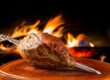 Cupim assado no espeto com fundo de churrasqueira, pronto para ser servido na Ramalho Experience em Campinas