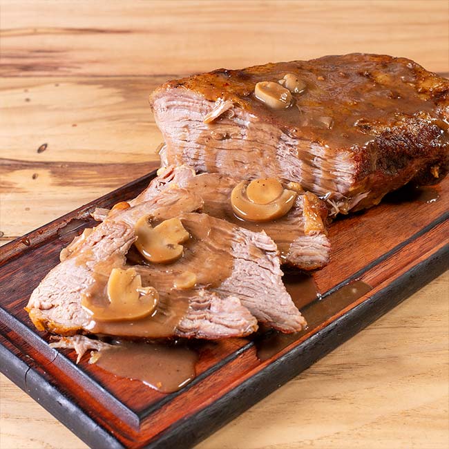 Carne Assada ao Molho com Champignon para Viagem Campinas – Ramalho Carnes Carne assada fatiada e suculenta coberta com molho madeira e champignon, servida em tábua de madeira. Opção de carne assada para viagem em Campinas da Ramalho Carnes.