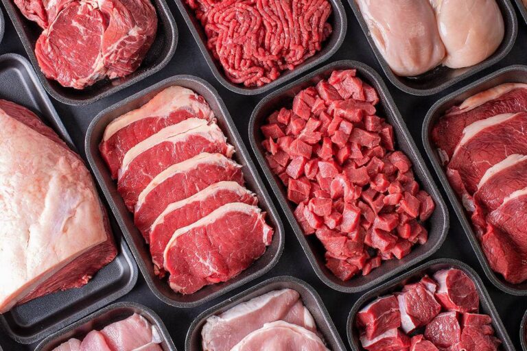 Vista superior de bandejas com cortes frescos e variados, ilustrando opções de carne boa e barata para churrasco e dia a dia.