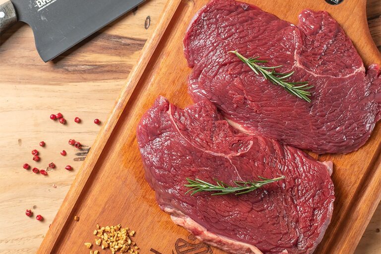 Quatro fatias frescas e suculentas de baby beef campinas dispostas sobre uma tábua de madeira artesanal na Ramalho Carnes.