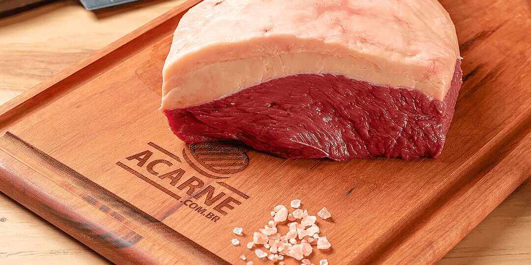 carne-boa-para-churrasco-guia-ramalho-carnes Picanha bovina premium com capa de gordura espessa e uniforme sobre tábua de madeira gravada com alecrim e sal rosa, uma verdadeira carne boa para churrasco.