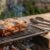 Uma peça suculenta de costela bovina, considerada uma ótima carne de segunda para churrasco, assando em uma grelha rústica sobre brasas de carvão com fumaça subindo.