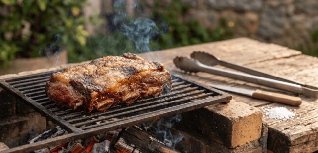 Costela Suculenta: O Potencial da Carne de Segunda para Churrasco Uma peça suculenta de costela bovina, considerada uma ótima carne de segunda para churrasco, assando em uma grelha rústica sobre brasas de carvão com fumaça subindo.
