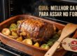 Peça suculenta de carne para assar no forno, dourada e rodeada por batatas rústicas em uma assadeira de cerâmica dentro do forno.