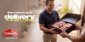 Homem sorridente recebendo na porta de casa uma caixa de delivery contendo cortes nobres de carne bovina e linguiças, encomendados no açougue online da Ramalho Carnes.