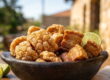 Uma tigela rústica de barro cheia de torresmo frito e pururuca crocante, servida com fatias de limão e um garfo sobre uma mesa de madeira, exemplificando o melhor torresmo de Campinas.
