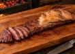 Fraldinha para churrasco assada inteira na tábua, com a capa de gordura dourada e as primeiras fatias mostrando o centro rosado